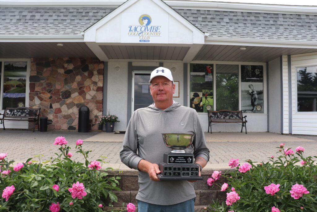 Tom McKinlay holding the Men's Mid-Master Trophy in front of his home course.